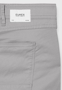 Graue Hose aus einem strukturierten Stoff, mit auffälliger Nähte, einer Gesäßtasche und einem weißen Etikett mit "EUREX by BRAX" sowie dem Jahr "1995."