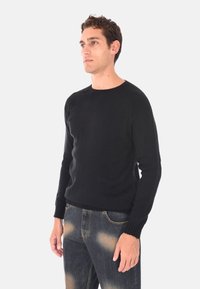 Maglione nero a maglia con collo rotondo, polsini e orlo a costine. Presenta una текстура morbida e una silhouette aderente. Abbinato a jeans strappati.