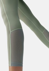 Világoszöld aktív leggings sima felülettel, hálós betétekkel és kontrasztos varrással a szegély és az oldal mentén a légáteresztőség érdekében.