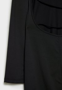 Robe noire sans manches avec fines bretelles suspendue à côté d'un vêtement noir à manches longues sur un fond clair.
