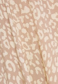 Béžová tkanina s texturovaným povrchem, která má abstraktní vzor bílé leopardí skvrny. Design zahrnuje různé tvary a velikosti skvrn.