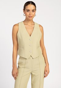 Lichtgroen, mouwloos vest met een diepe V-hals, vijf knopen en zijzakken. De stof heeft een subtiele textuur en een getailleerde pasvorm.