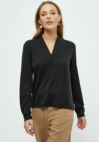 Sort langærmet top med V-hals design, lavet af et glat stof. Har en lige pasform og minimale syninger. Kombinationen med beige bukser.