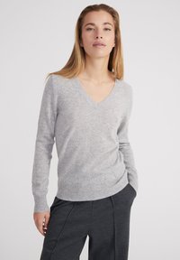 Grauer V-Ausschnitt-Pullover aus weichem Strickgewebe. Mit langen Ärmeln und ribbed Saum. Kombiniert mit dunkelgrauen Hosen für einen Kontrast.