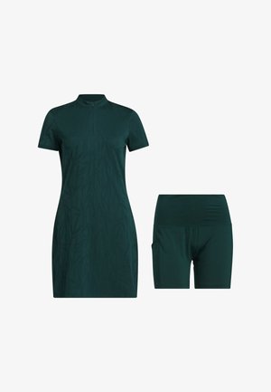 Set di abbigliamento sportivo a due pezzi composto da un vestito verde scuro a maniche corte con colletto a zip e pantaloni corti coordinati. Il tessuto è liscio con una leggera texture.