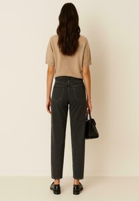 Grijze high-waisted jeans met een rechte pijp en achterzakken, gecombineerd met een beige, kortdriekwarts mouw trui en een zwarte handtas. Platgeschikte schoenen worden gedragen.