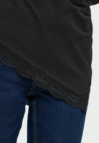 Haut noir avec bordure en dentelle festonnée associé à un jean en denim bleu, visible de la taille jusqu'à mi-cuisse.