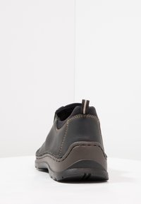 Zwarte leren schoen met bruine stiksels, ronde vorm, textiel rondom de kraag, en een lusje aan de achterkant. Rubberen zool.