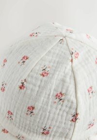 Baumwollmütze mit gesteppter Textur und hellem floralen Muster in Pink auf weißem Hintergrund; verfügt über eine sechsteilige Konstruktion und genähte Nähte.