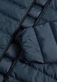Giacca a vento trapuntata blu navy con un esterno liscio, caratterizzata da una zip prominente e un dettagli di tasca imbottita.