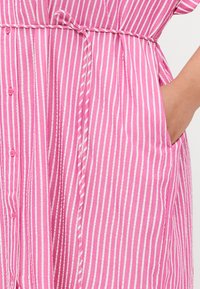 Ροζ και λευκό ριγέ φόρεμα πουκάμισο με κοντά μανίκια, κλείσιμο με κουμπιά, σφικτή μέση και πλαϊνές τσέπες. Μαλακή βαμβακερή υφή, χαλαρός σχεδιασμός.