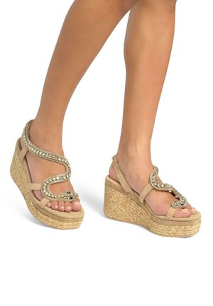 Sandali con zeppa beige con base in paglia intrecciata, caratterizzati da una fascia curva decorata con strass e un cinturino alla caviglia sicuro.