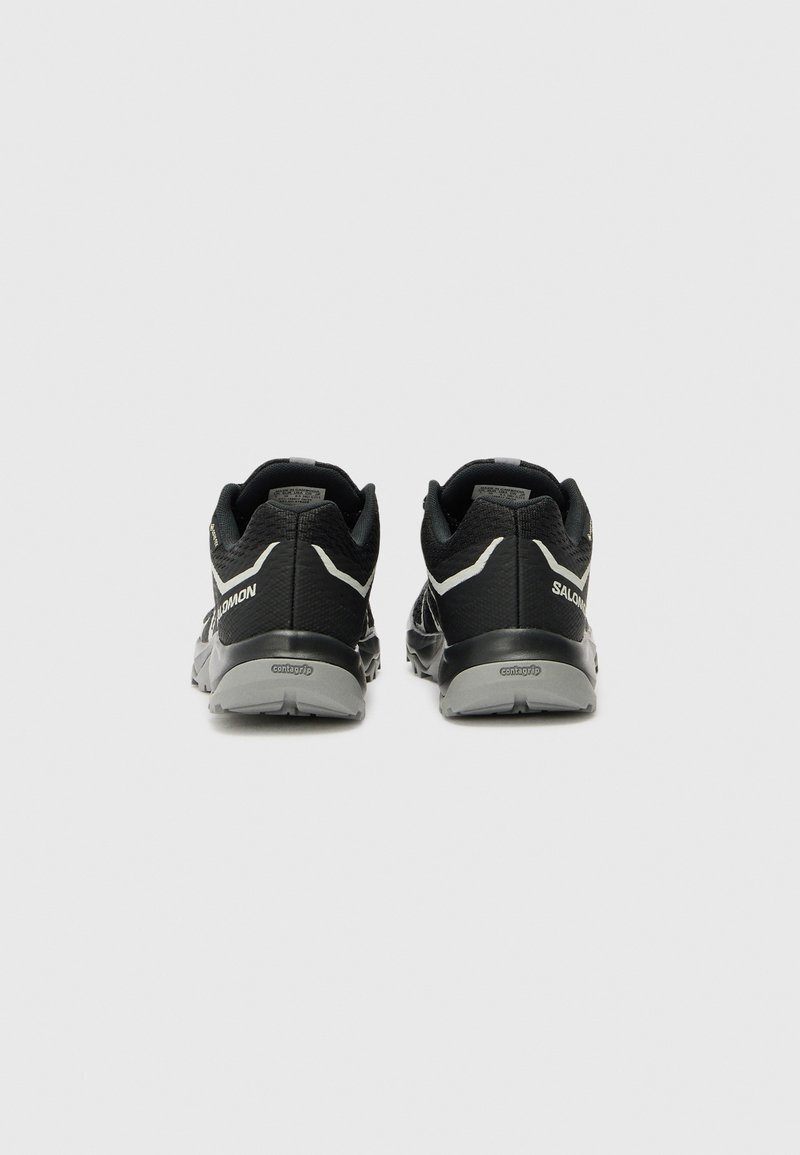 Schwarze Trailrunning-Schuhe verfügen über ein strukturiertes Mesh-Obermaterial, eine unterstützende Ferse und eine graue Gummisohle mit einem ausgeprägten Profil.