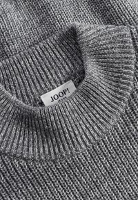 Gray knitted sweater with a ribbed texture and a high collar. Features a label with the brand name "JOOP!" in black on a white background.
