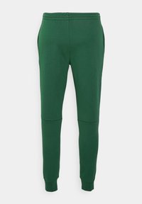 Pantalon de survêtement vert en tissu doux avec une taille élastique, des jambes fuselées et des détails de panneaux contrastants aux genoux. Deux poches latérales visibles.