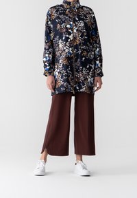 Granatowy kwiatowy długi żakiet z zapięciem na zamek, w połączeniu z brązowymi spodniami w szerokim kroju, z bocznymi zamkami. Całość uzupełniają białe trampki.