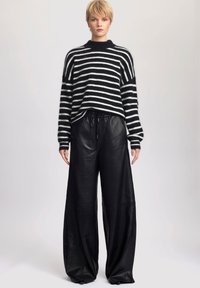 Neulottu musta-valkoinen raidallinen villapaita, jossa on pyöreä pääntie, yhdistettynä leveisiin mustiin nahkahousuihin, joissa on joustava vyötärö.