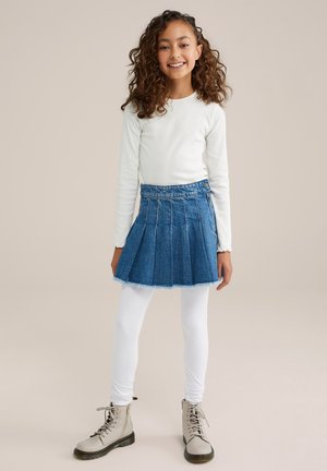 Blauer Denim-Faltenrock mit fransigem Saum, kombiniert mit weißen Leggings und hellgrauen, geschnürten Kampfboots. Langärmliges weißes Shirt.