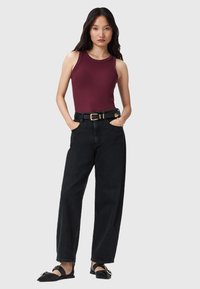 Top sin mangas color burdeos, jeans anchos de tiro alto color negro con bolsillos frontales, sandalias negras con acentos dorados, diseño minimalista.