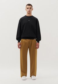 Felpa nera con collo rotondo, caratterizzata da un piccolo logo, abbinata a pantaloni larghi color senape e sneakers bianche.