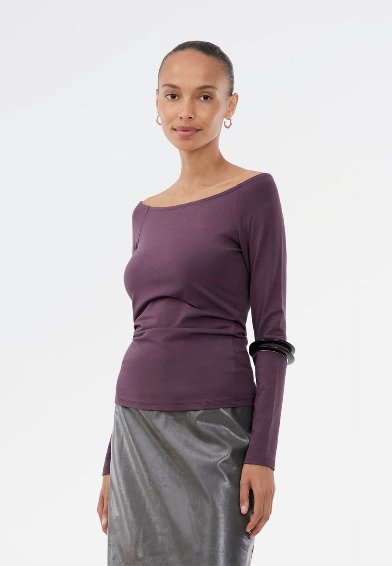 Purple long-sleeve top with an off-shoulder design, made of a soft, smooth fabric, paired with a shiny gray midi skirt.