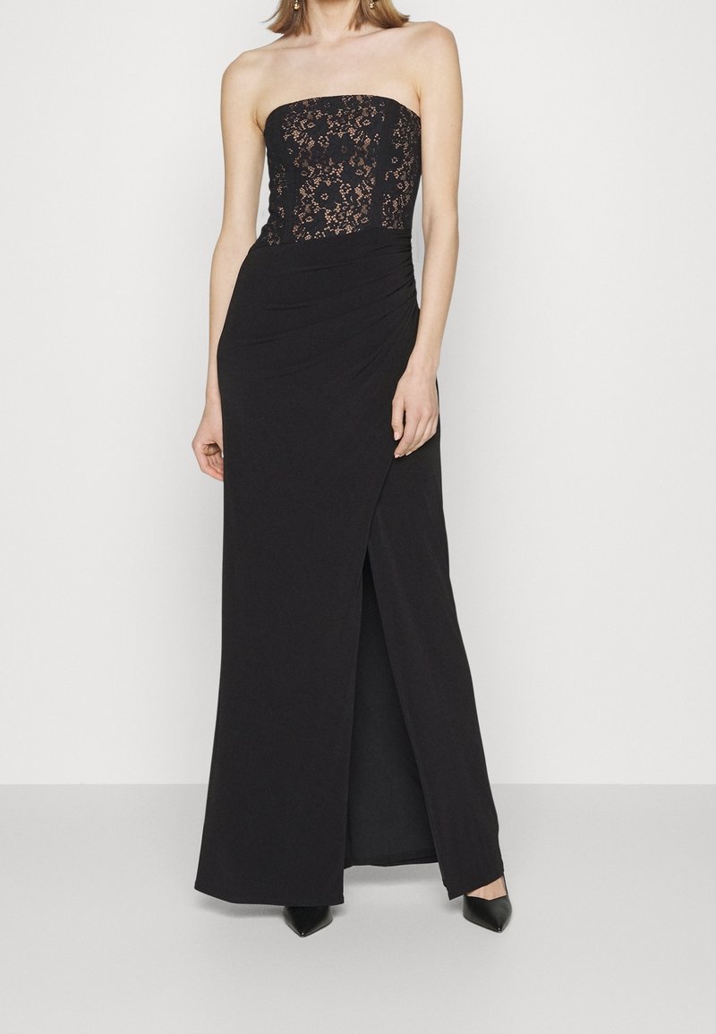 Svart ärmlös klänning med spetsöverdel, rynkad midja och hög slits. Slät tyg med en figurnära silhuett.