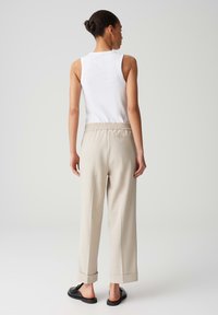 Beige op maat gemaakte broek met een elastische tailleband, opgerolde boorden, gecombineerd met een witte tanktop. Zwarte sandalen maken de outfit compleet.