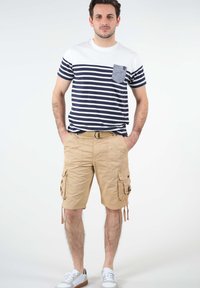 T-shirt à manches courtes rayé bleu marine et blanc avec une poche poitrine, associé à un short cargo beige avec des poches latérales et des liens ajustables. Baskets blanches.