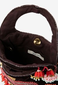 Sac en tissu marron avec des accents de perles décoratives, une bordure à motifs et une fermeture à pression. L'intérieur montre une étiquette et une texture douce.