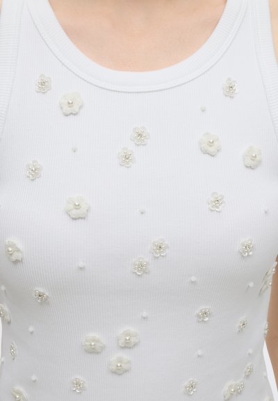 Haut sans manches blanc en maille côtelée avec petites applications florales blanches et centres en perles et perles à l'avant.