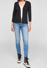 Black long-sleeve cardigan with open front, paired with light blue skinny jeans and high-top sneakers featuring tan and white accents.