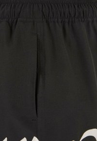 Sorte shorts med elastisk liv, der har en sidelomme og hvid grafisk design ved kanten. Glat stofstruktur.