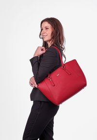 Červená kožená taška přes rameno s dvojitými horními uchy, strukturovaným tvarem a zvýšeným detailem loga. Texturovaný povrch s elegantními, minimalistickými kovovými akcenty.