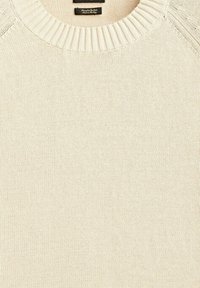 Pull tricoté de couleur crème avec un col rond côtelé et une étiquette visible à l’intérieur du col.