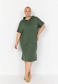 Vestido verde con capucha, hecho de una tela suave, que presenta un bolsillo frontal y mangas cortas, con aberturas laterales para mayor facilidad de movimiento.