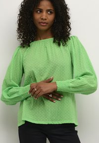 Blouse verte texturée avec des manches bouffantes, orn�ée d'un motif à pois et de poignets élastiques. Coupe décontractée avec un col rond.