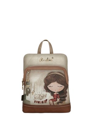 Mochila pequeña en tonos beige y marrón, con una niña caricaturesca de ojos cerrados y el texto "Conócete a ti mismo" en el bolsillo delantero.