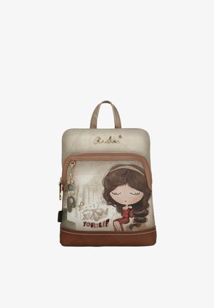 Mochila pequeña en tonos beige y marrón, con una niña caricaturesca de ojos cerrados y el texto "Conócete a ti mismo" en el bolsillo delantero.