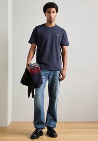 Ναυτικό κοντομάνικο μπλούζα με λαιμόκοψη, σε συνδυασμό με ανοιχτό μπλε ίσιες τζιν παντελόνι. Κρατάει μια patterned, σκούρα κουβέρτα.