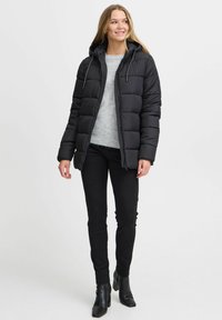 Svart puffjacka med huva, vadderad design och dragsnören; ihop med en grå tröja och svarta byxor; bärs med svarta klackstövlar.