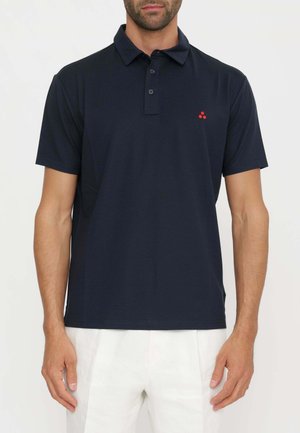 Mann trägt ein marineblaues kurzärmeliges Poloshirt mit kleinem rotem Logo auf der linken Brust und weiße Hose.