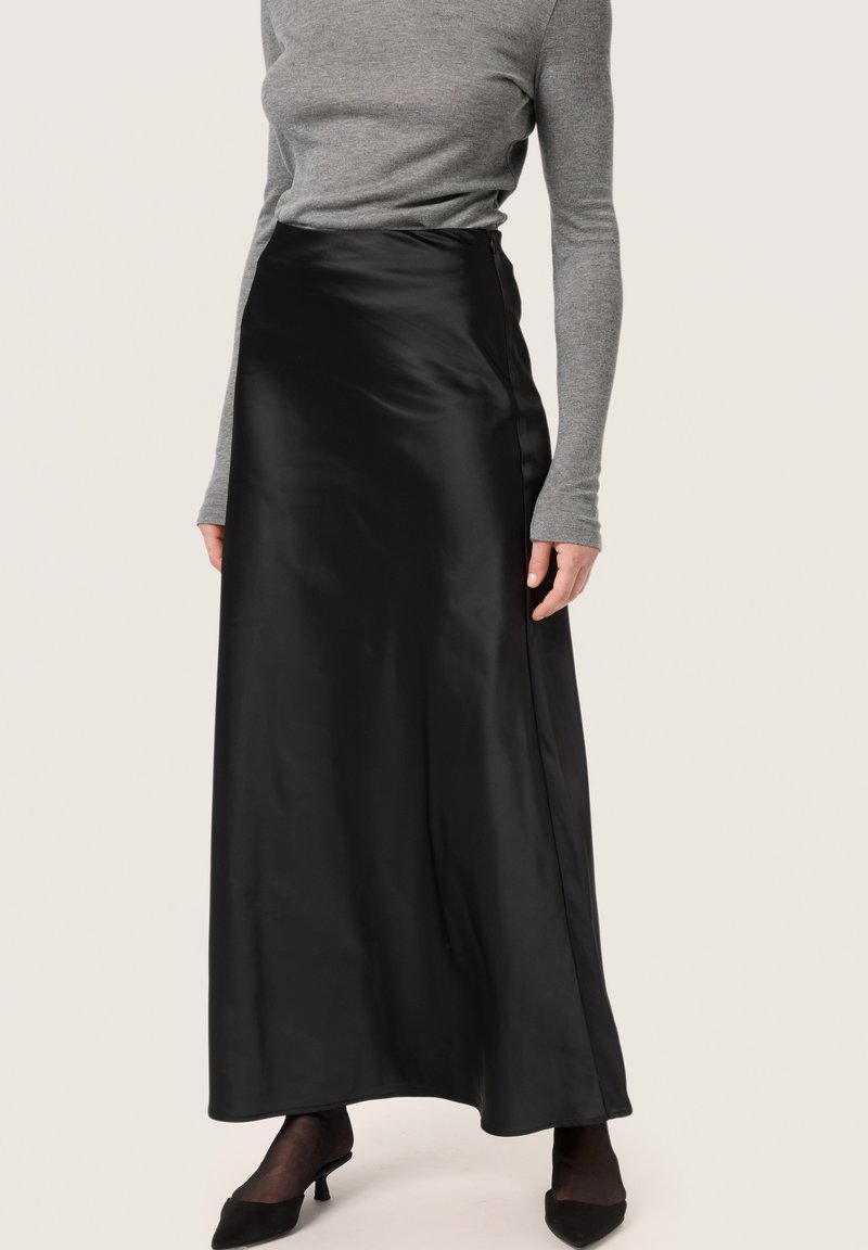 Schwarzer Satin-Maxikleid mit glatter Textur und feinem Glanz, ausgestattet mit einer taillierten Taille und einem fließenden, eleganten Fall. Kombiniert mit einem grauen Langarmoberteil.