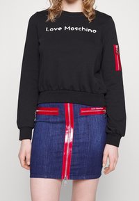 Černá mikina se textem "Love Moschino", spárovaná s modrou džínovou sukní s červenými lesklými zipy a akcenty.
