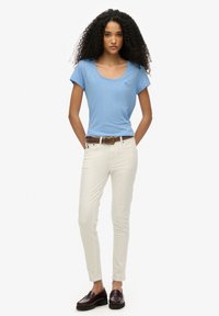 Jasnoniebieska koszulka z krótkim rękawem i dekoltem w kształcie litery "scoop", zestawiona z dopasowanymi kremowymi dżinsami i ciemno bordowymi loafersami. Płaskie buty, bez widocznych logo.