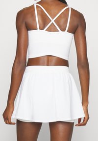 Biały sportowy top z krzyżującymi się ramiączkami, zestawiony z białą, rozkloszowaną spódnicą, oba wykonane z gładkiego, lekkiego materiału.