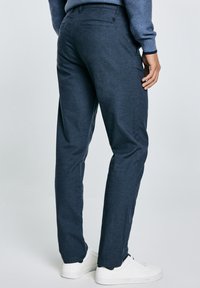 Pantalones azul marino de corte slim, hechos de una tela texturizada, que cuentan con un bolsillo trasero y se llevan con zapatillas blancas.