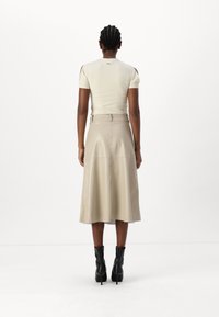 Beige Leder-Midirock mit ausgestelltem Design, ausgestattet mit einem Bund und einem Gürtel sowie dezenten Nahtdetails; kombiniert mit schwarzen, schuhe mit Absatz.