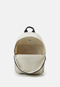 Krämfärgad ryggsäck med svart handtag, öppen huvudfack som visar ett litet innerfack och en Tommy Jeans-lapp inuti.