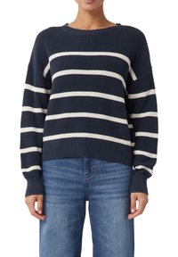 Sweter w paski w odcieniach granatu z białymi poziomymi paskami, z okrągłym dekoltem, żebrowaną teksturą i długimi rękawami; w połączeniu z jasnoniebieskimi dżinsami.