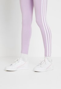 Leggings lilla chiaro con strisce bianche sui lati abbinati a scarpe da ginnastica bianche con dettagli rosa e suola testurizzata.